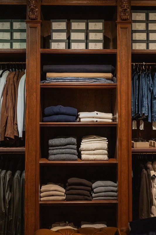 A wooden shelving unit with folded sweaters and shirts, and hanging jackets.