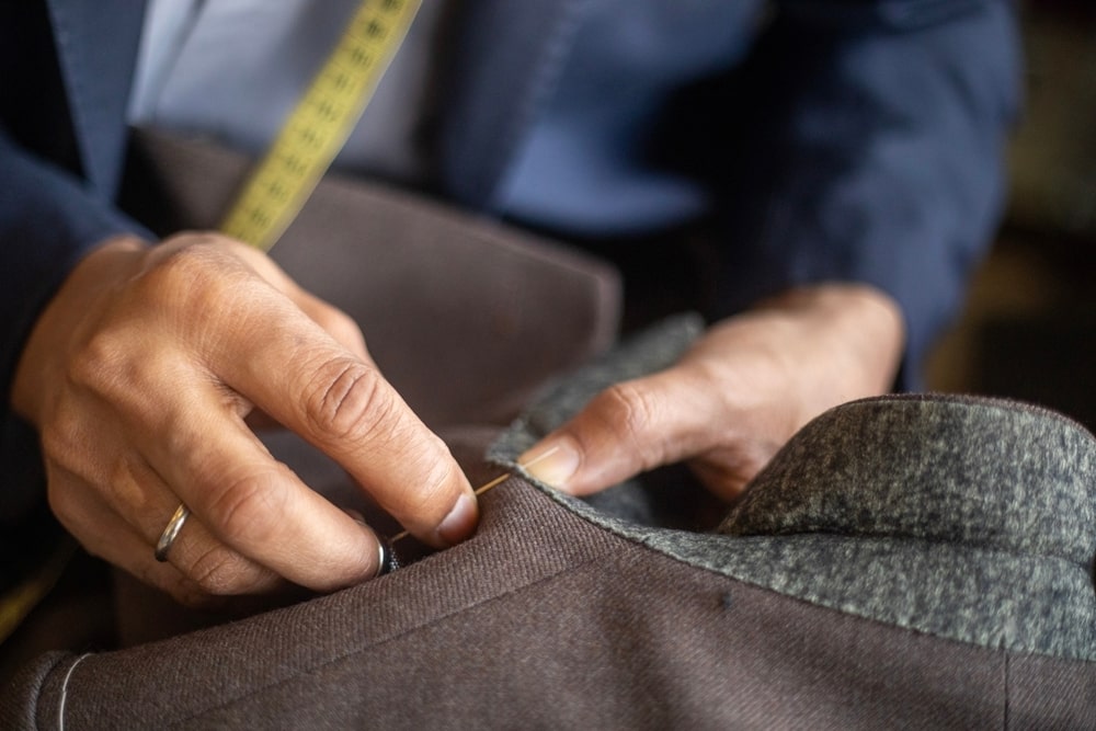 Tailor sewing a suit with a measuring tape around their neck.