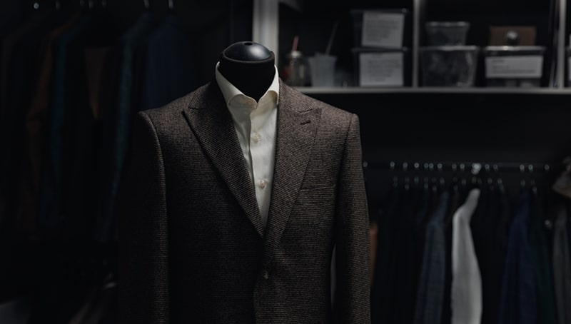Mannequin wearing brown suit jacket and white shirt in a closet.