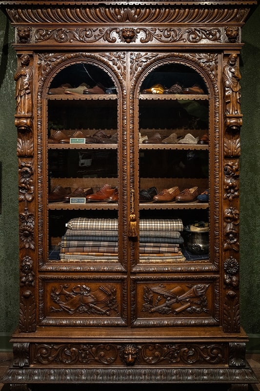 Ornate wooden cabinet with glass doors, displaying shoes and clothing.
