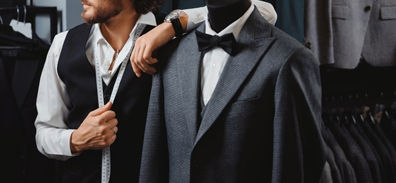 Tailor measuring a suit on a mannequin.