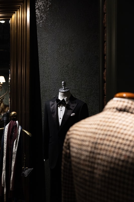Mannequin wearing a black tuxedo in a dimly lit room.