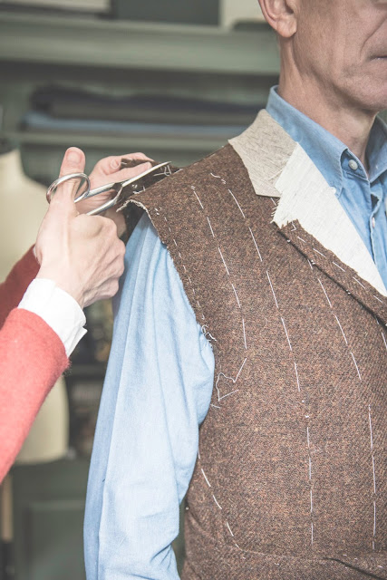A tailor adjusting a bespoke jacket during a fitting